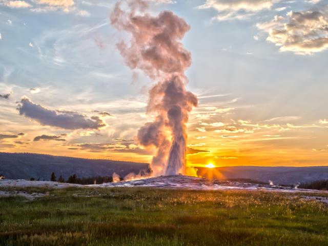 Geyser erupting with sun setting in the background
