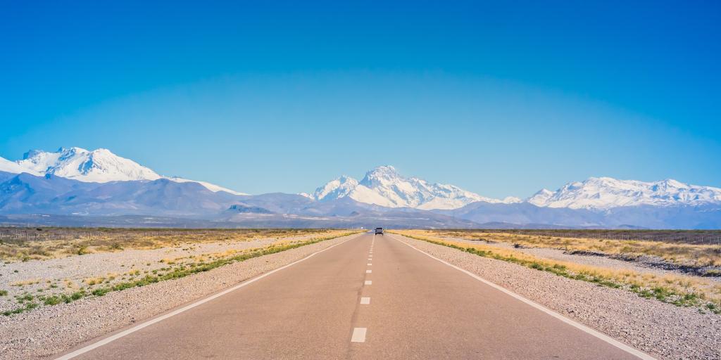 A car on an empty road in Mendoza, Argentina, with mountains in the background