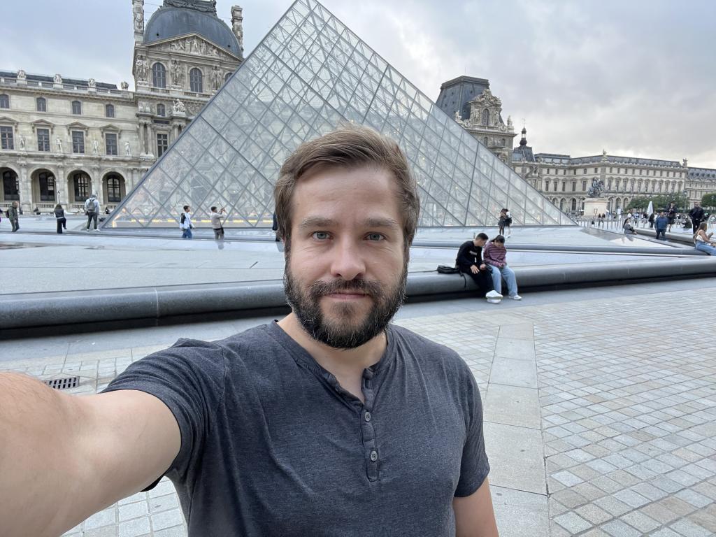 Sasha Yanshin standing in front of the glass pyramid at the Louvre Museum in Paris, France.