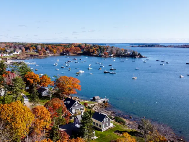 Aeriel image taken with a drone of the coastal Maine town with autumnal trees and residential buildings and boats docked in the bay in the distance