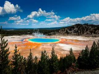 A panoramic view of the Grand Prismatic Spring in Yellowstone National Park show's that the water's color is a mix of orange, yellow, green, and blue.