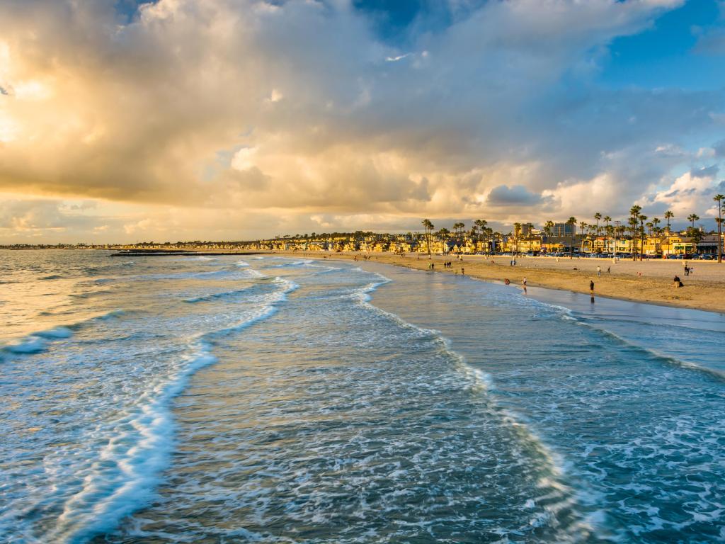 Newport Beach, California, USA with waves in the Pacific Ocean in the foreground and a view of the beach at sunset.