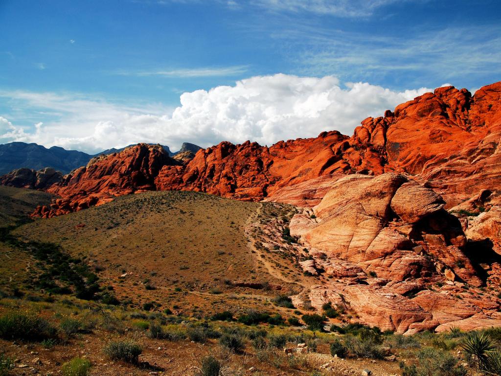 Red Rock Canyon viewed from a height looking towards the bright red canyons in the distance against a blue sky. 