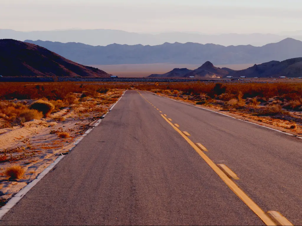 An empty Interstate 40 along Needles Freeway in Mojave National Preserve with a view of mountains on a hazy afternoon.
