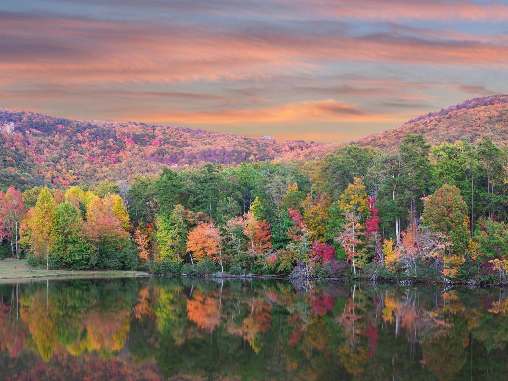 Cheaha State Park, Alabama, USA with a panorama of the beautiful fall foliage reflected in the lake, trees and hills in the distance at sunset.