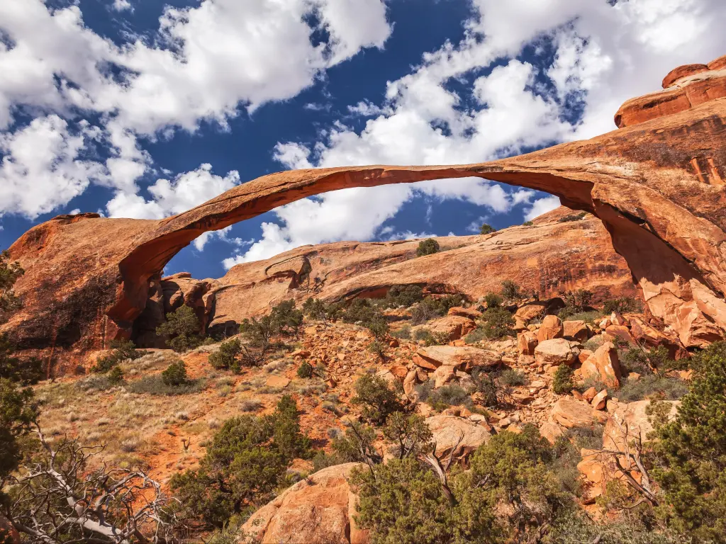 Wide view of Landscape Arch, a thin and long rock formation against blue sky dotted with clouds, Arches National Park, Utah, USA