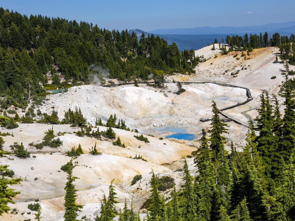 Bumpass Hell, which is the largest hydrothermal site in Lassen Volcanic National Park, on a sunny day with forested hills in the background
