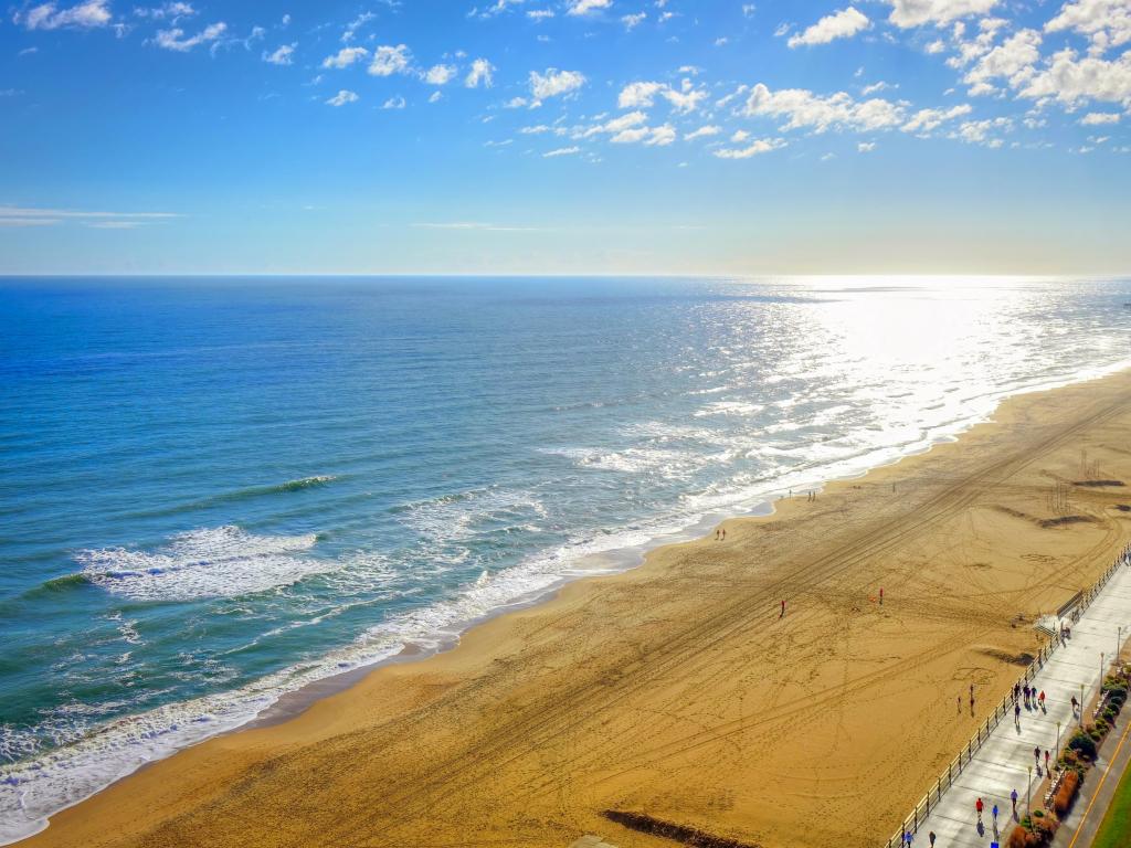 Virginia Beach, Virginia, USA with the beach boardwalk in the foreground and taken as a high aerial panoramic view of the yellow sand, calm sea on a clear sunny day.