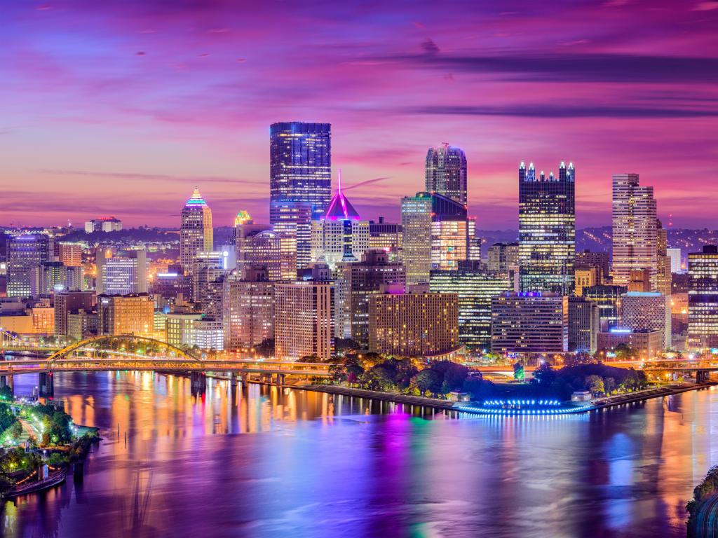 Pittsburgh, Pennsylvania, USA with the city skyline in the distance taken at sunset with a purple sky and the city reflecting in the water in the foreground.