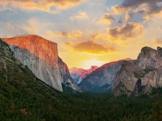 View of steep sided cliffs and green forested valley with pink sunset light