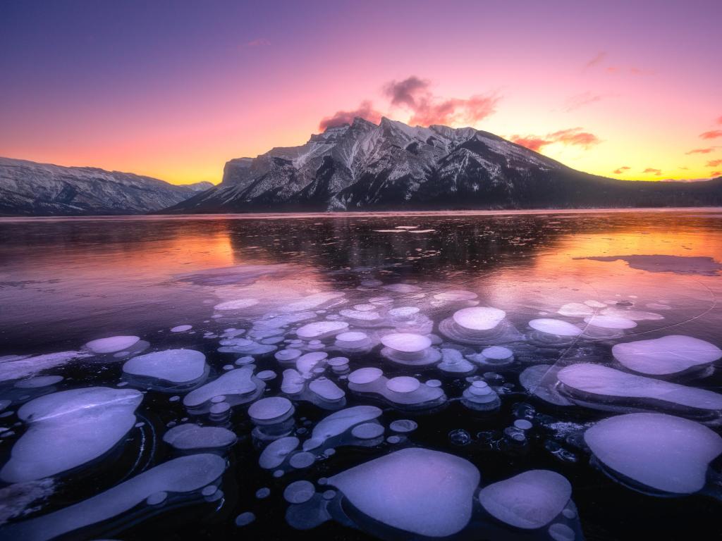Ice bubbles on the surface of the blue ice. Frozen lake in winter mountains. Minnewanka Lake, Alberta, Canada
