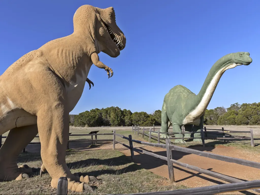 Two giant dinosaurs figures stand at the Dinosaur Valley State Park, Texas, with a blue sky behind