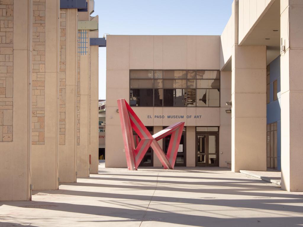 The sand colored exterior of the museum with a red colored abstract sculpture