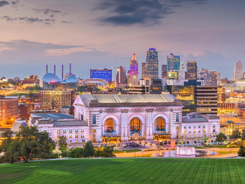Kansas City, Missouri with the downtown skyline with the Union Station at dusk and green grass in the foreground. 