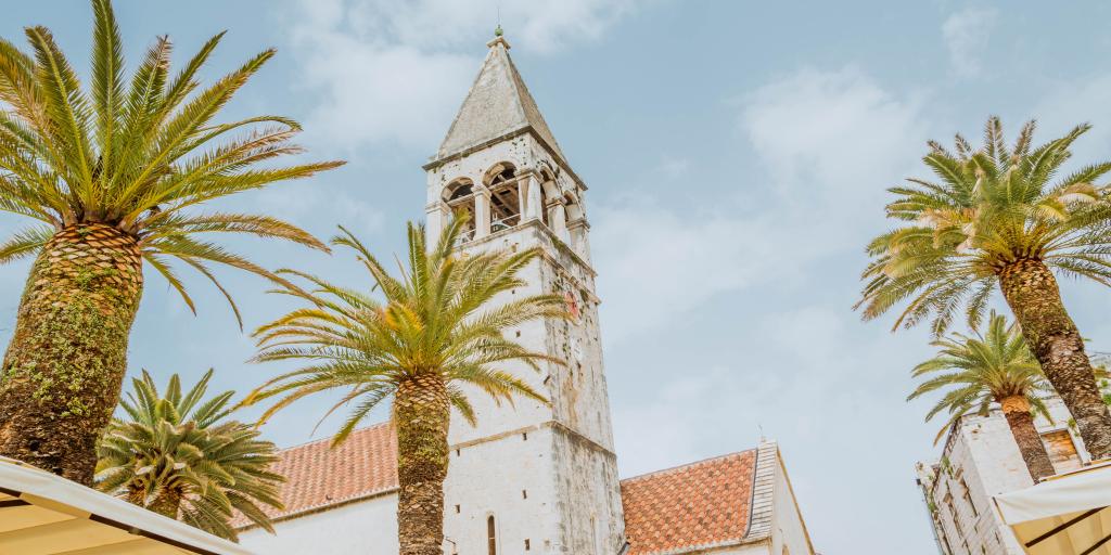The tower of St Lawrence Cathedral in Trogir, Croatia, with palm trees in the foreground