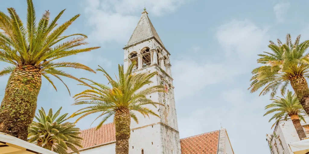 The tower of St Lawrence Cathedral in Trogir, Croatia, with palm trees in the foreground
