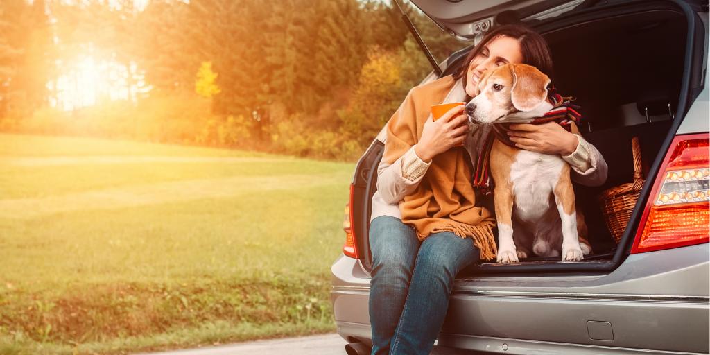 A woman taking a break with her dog sitting in the boot of the car 