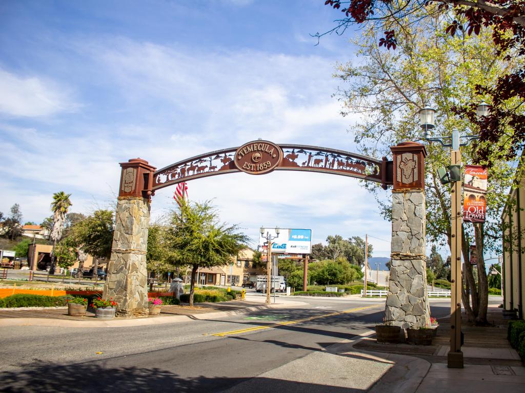 Entrance sign across archway to Old Town Temecula, with shops and gardens in the background