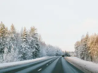 A car driving down the right side of a road surrounded by snowy trees