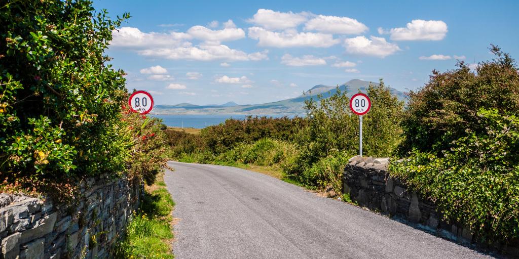2 speed limit signs on a country road with mountains in the background in Ireland 