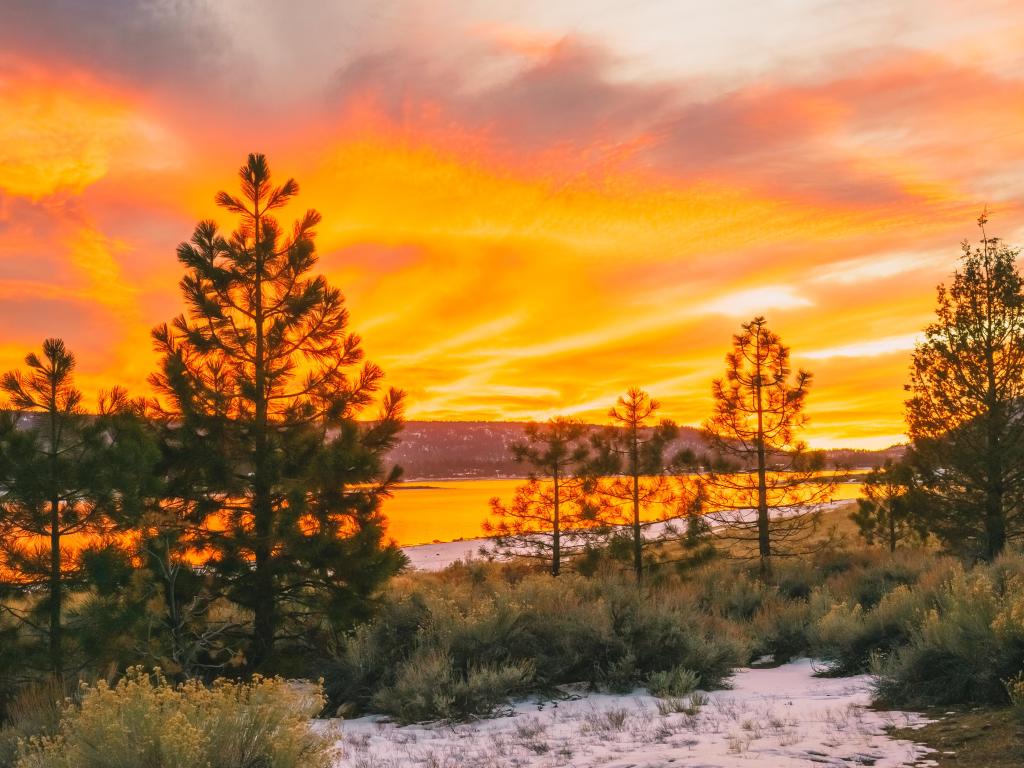 Sunset over Big Bear Lake in winter, casting an orange glow in the sky with snow all around