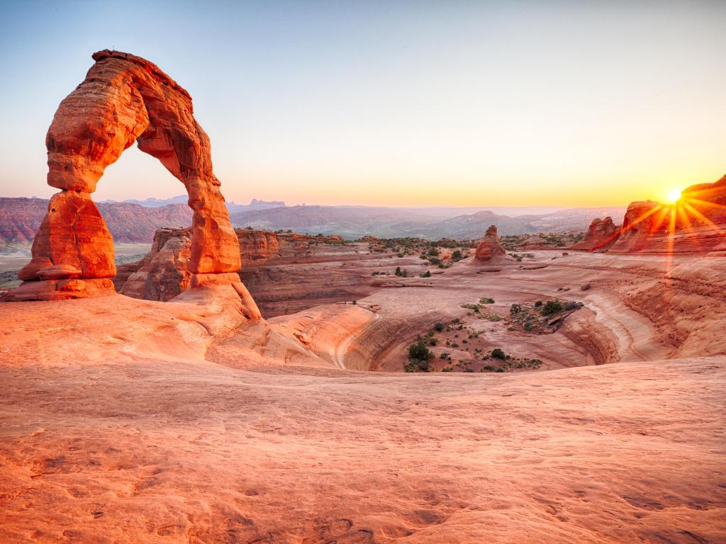 Sun setting in the horizon in Arches National Park with Delicate Arch in view