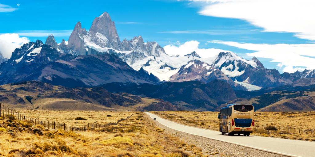 A bus driving along a deserted road towards some snow-capped mountains in Argentina 