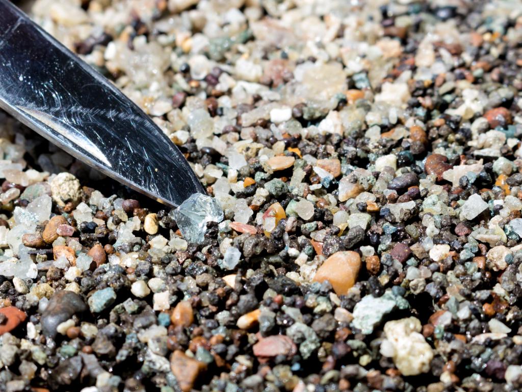 Close up image of a lifting a piece of clear stone out of many colorful small pebbles
