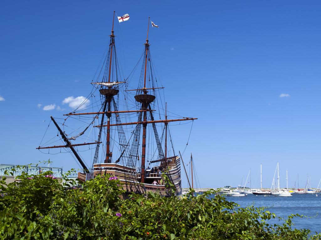 Plymouth, Massachusetts, USA with a replica of the Mayflower ship taken on a sunny day with other boats in the distance. 