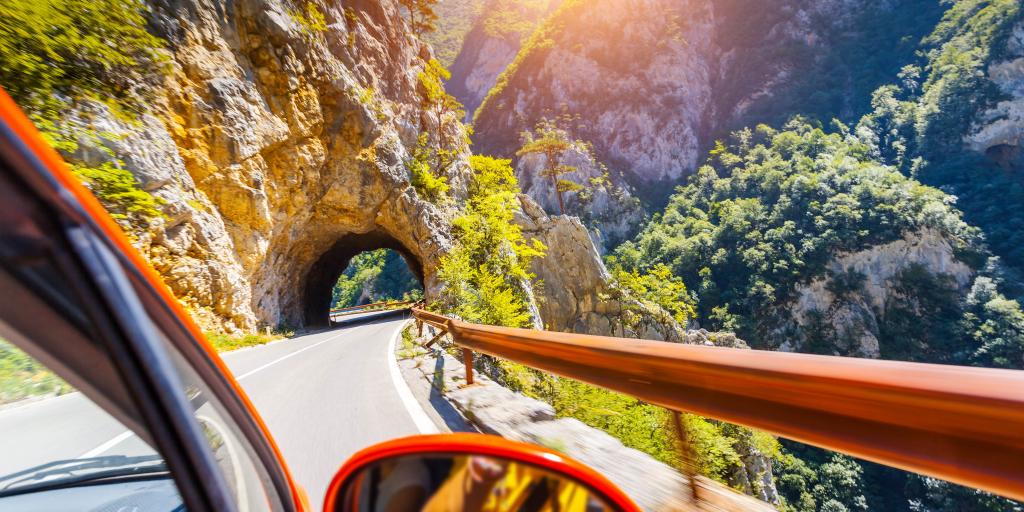 Edge of a red car going through a mountain tunnel on a sunny day