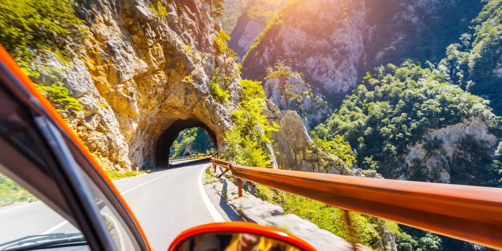 Edge of a red car going through a mountain tunnel on a sunny day