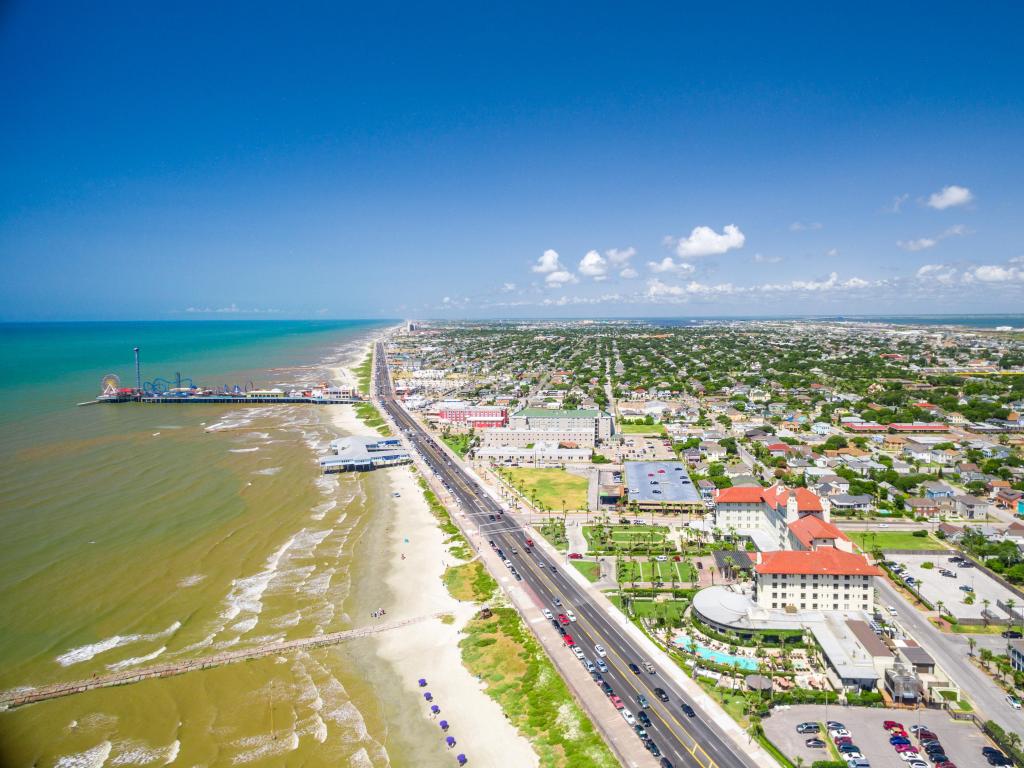 Galveston Island, Texas taken as an aerial photo with the sea and beach on one side and the town on the other separated by a road on a clear sunny day.