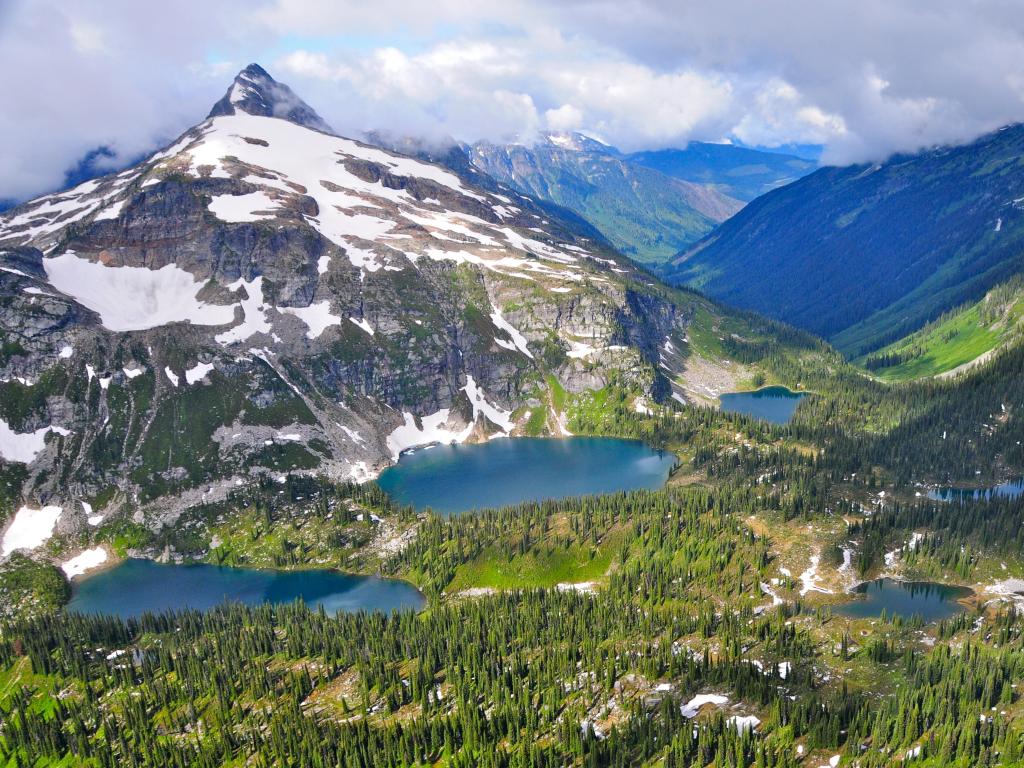 Snow-capped, cloud-covered mountains with forests and lakes in the valleys