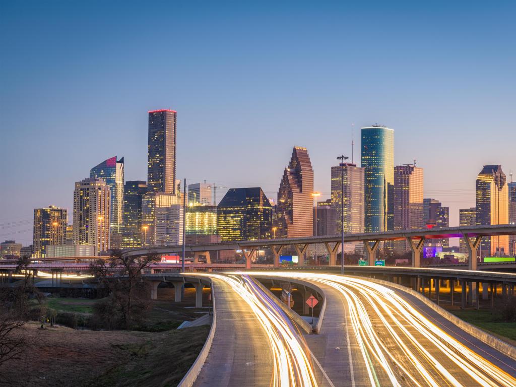 Houston, Texas, USA downtown city skyline and highway at night, with the buildings in the distance and the road in the foreground lit up.