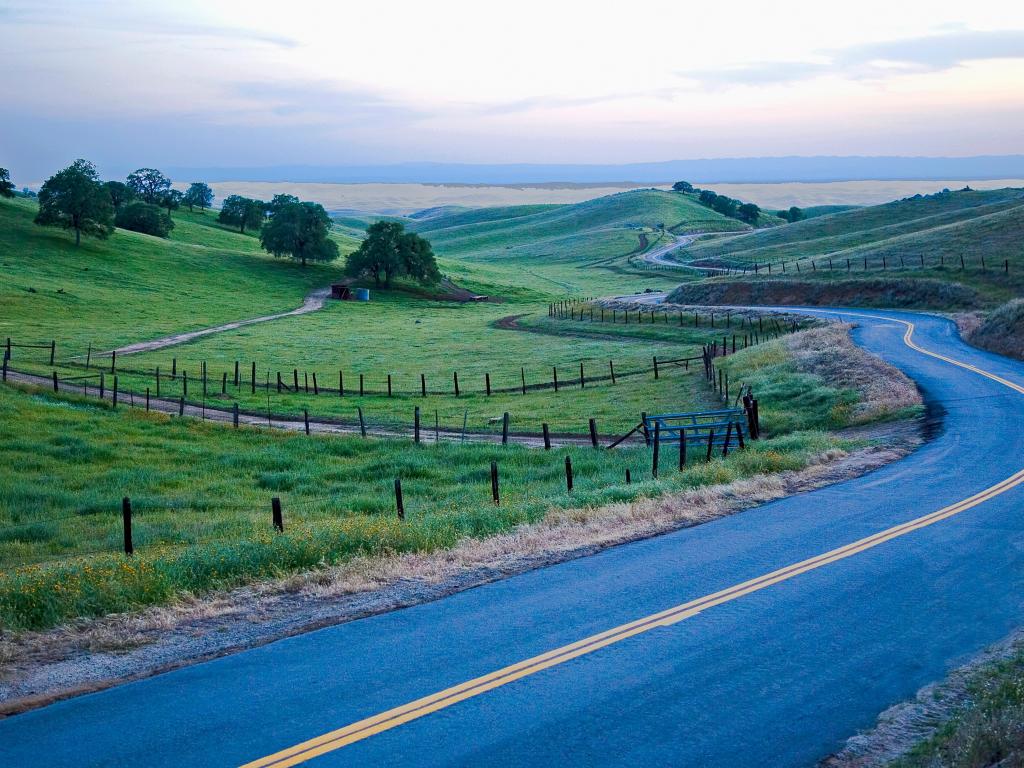Bakersfield, California, USA with a road in erasing evening amongst farm land and hills. 