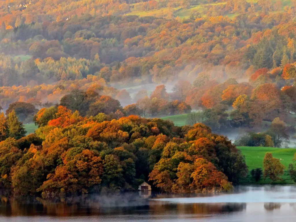 A morning mist rolls over the colourful trees and glittering Lake Windermere in the Lake District