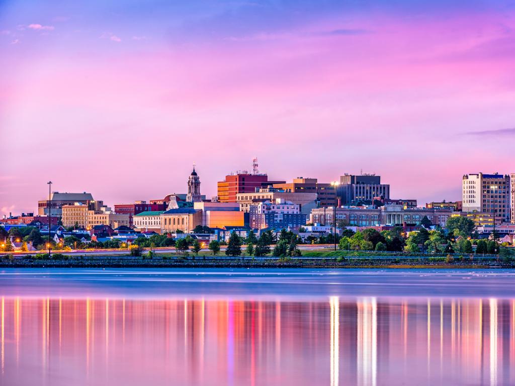 Portland, Maine at sunset with the downtown skyline in the background below a pinky sky and reflecting in the water in the foreground.