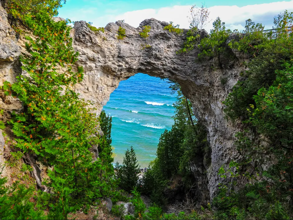 A picturesque view of Lake Huron through a natural Arch Rock with wedges growing in the walls on Mackinac Island Michigan in a sunny morning