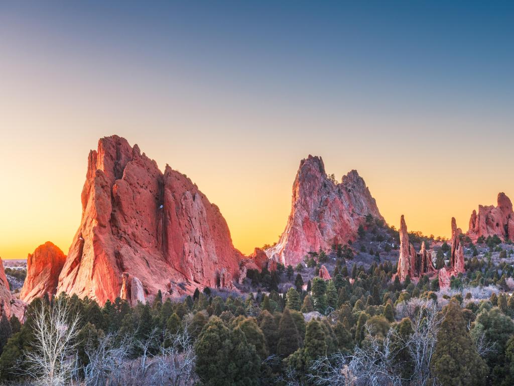 Garden of the Gods, Colorado Springs, Colorado, USA with trees in the foreground and the tall cliffs against a sunset sky.