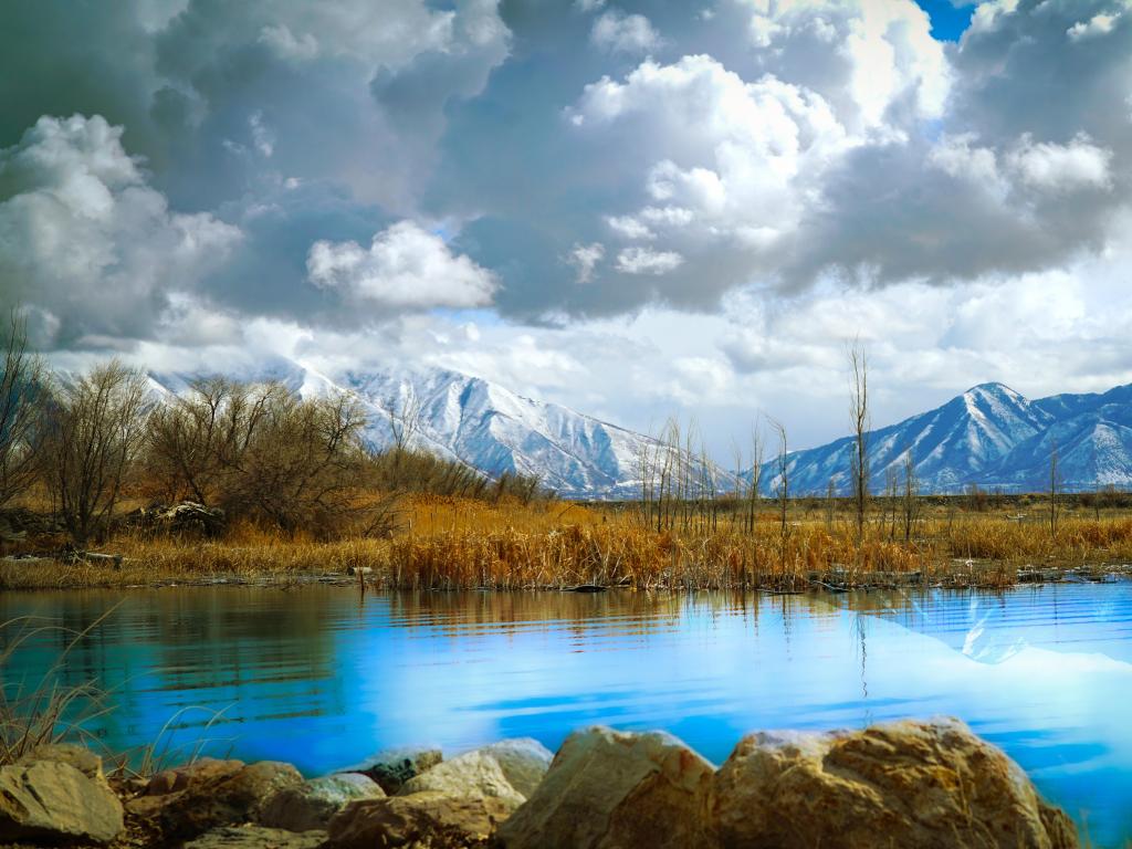 Utah Lake, Utah Lake State Park, Provo, Utah, USA with a stunning mountain view over Utah Lake, snow-capped mountains in the distance and clouds above.