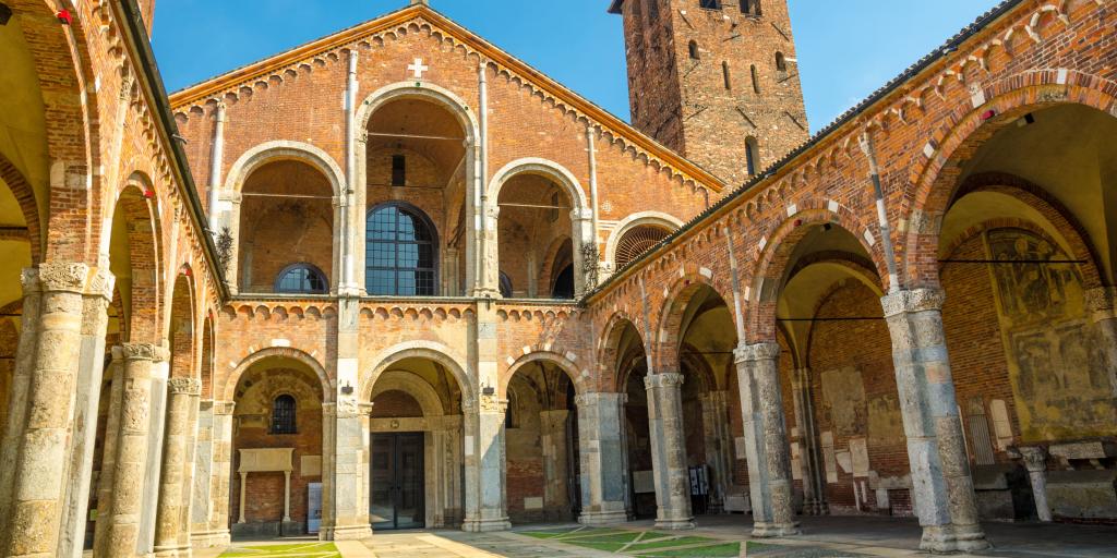 Basilica of Sant'Ambrogio church in Milan, Italy, with bell towers, courtyard, arches, and blue sky background