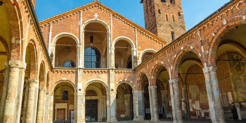 Basilica of Sant'Ambrogio church in Milan, Italy, with bell towers, courtyard, arches, and blue sky background