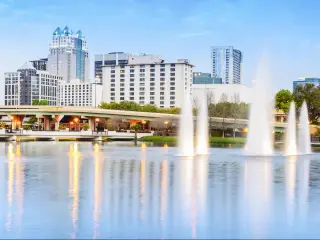Orlando, Florida, USA with the downtown Orlando skyline in the distance with Lake Eola Park in the foreground and a water feature to the right.