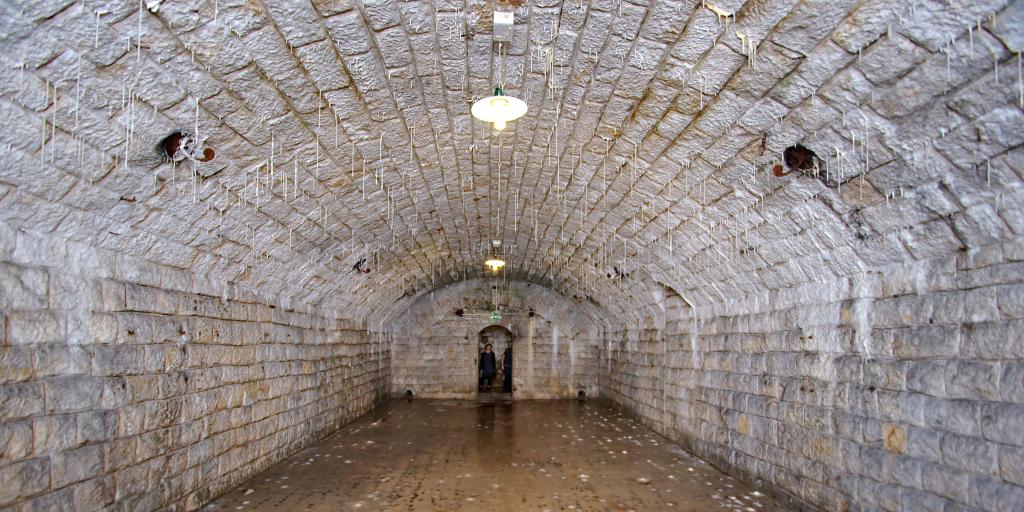 A white curved room inside Fort Douaumont, France, with stalagmites hanging from the ceiling 