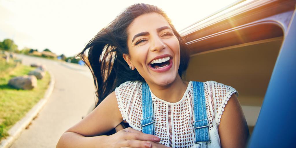 Cheerful young woman with brown hair enjoying the fresh air with hear head outside the window of a car as it speeds down winding road