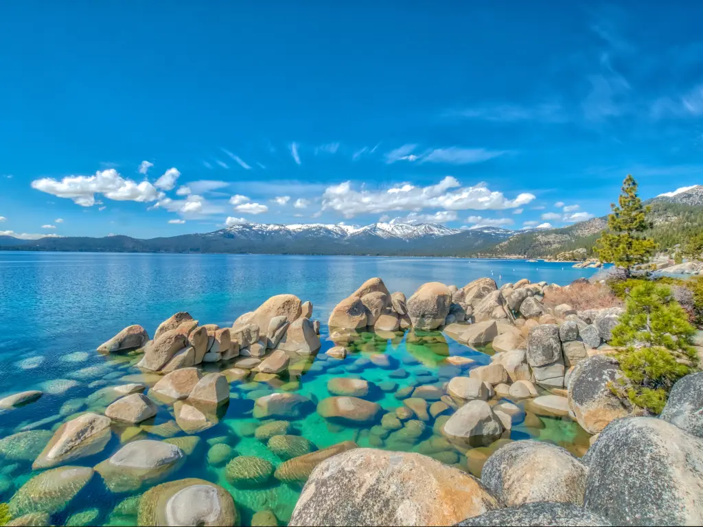 Rocks and pristine water of Lake Tahoe with snow-capped mountains in the background.