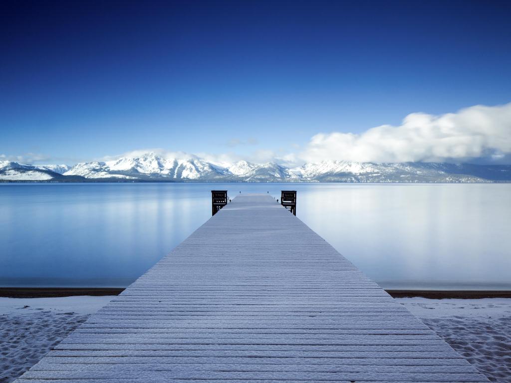 A snowy pier at Lake Tahoe with snowy mountains in the background on a clear winter day.
