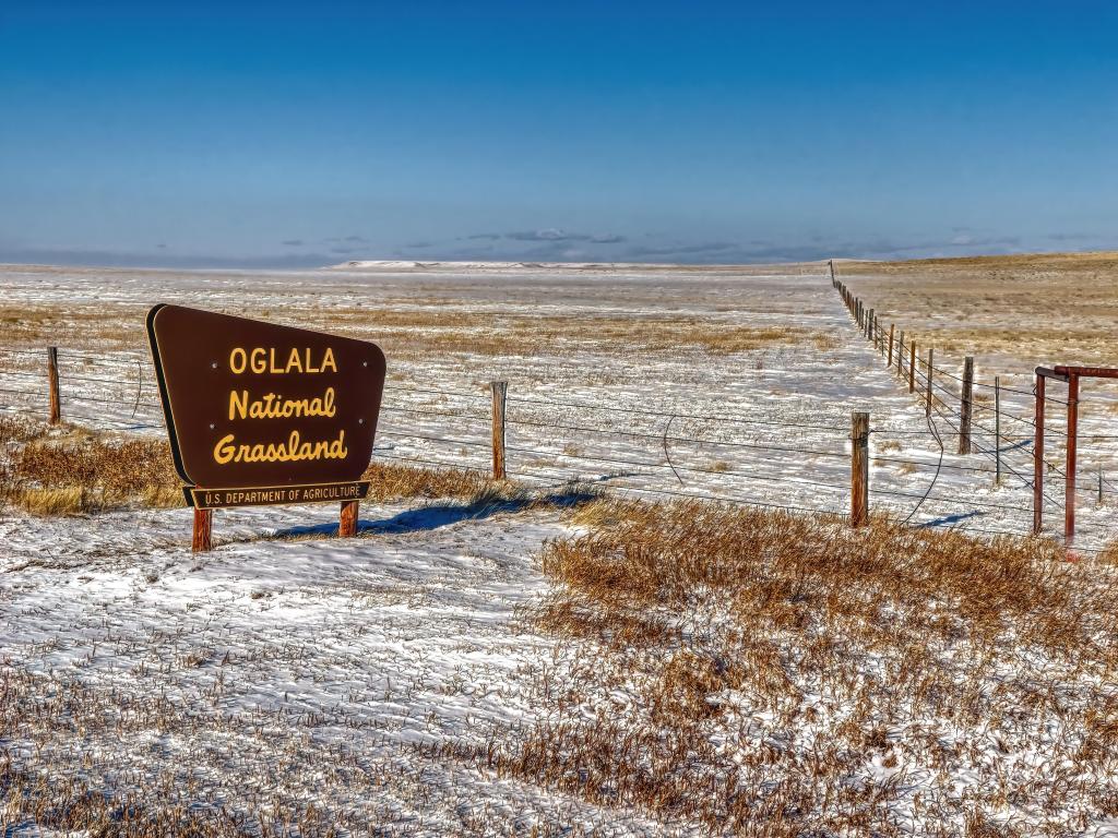 Expansive view of Oglala National Grassland in the winter, with a wooden sign in the foreground and a dusting of snow on the flat ground