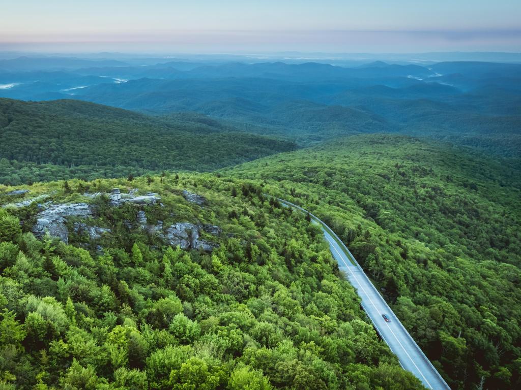 Aerial view of the Blue Ridge Parkway at Rough Ridge Lookout, with lush dense forest surrounding the winding road