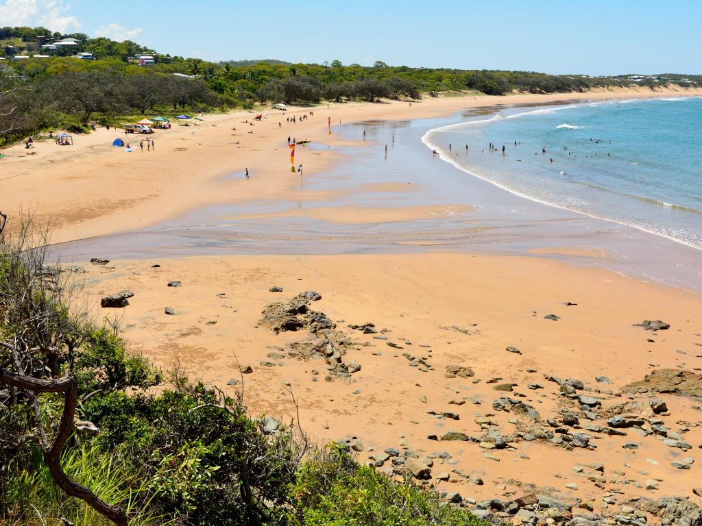 Uncrowded beach with deep golden sand, turquoise water and green vegetation reaching down to the edge of the sand